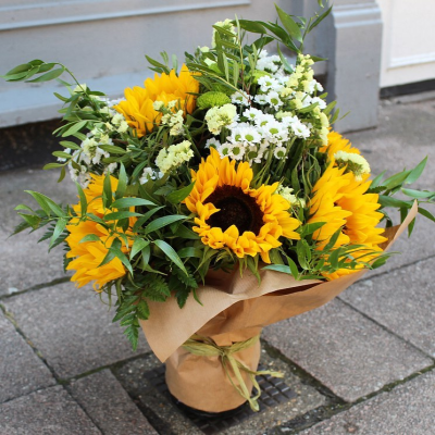 Golden Glow - Brighten someone's day with the `Golden Glow` arrangement, featuring a stunning sunflower mix with seasonal blooms. Complemented by lush green foliage, this arrangement brings a touch of nature's radiant beauty into any space.